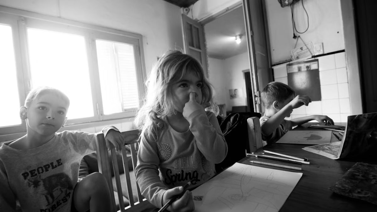 Three children drawing at a table in grayscale, indoors, natural light.